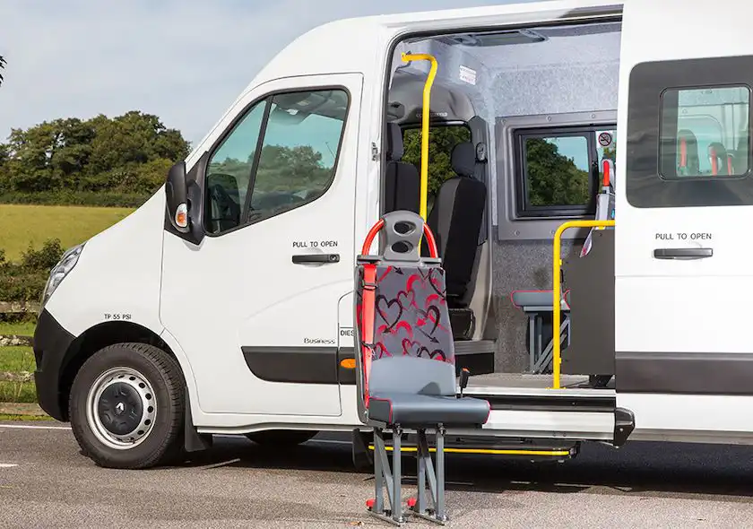 Close-up of a white minibus with its sliding side door open, displaying removable seats and tracked flooring inside.